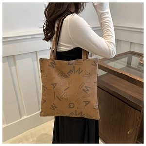 Close-up of brown leather tote bag with letter prints and fine stitching detail
