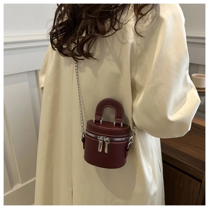Detail showing the burgundy leather bucket bag with white stitching and silver chain strap