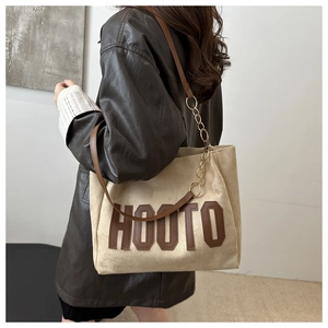 Dettaglio della borsa tote kaki con patch HOOTO in pelle e catena dorata
