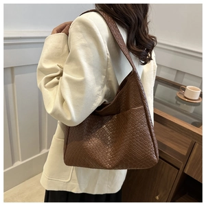 Close-up of caramel brown woven tote bag with wide shoulder strap worn by a model