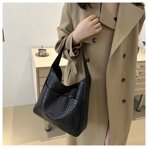 Detail of a large black woven PU leather tote bag worn with a stylish khaki trench coat