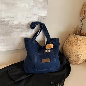 Large blue denim tote bag with leather logo patch and plush charm in an artistic setting