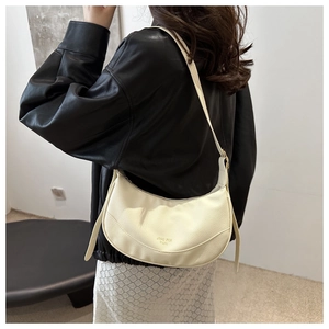 Detail of minimalist cream crescent bag showing premium pebble grain leather and gold logo