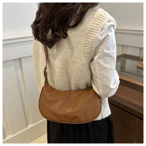 Detail of a brown lychee-textured leather hobo bag with gold lettering shown on a model