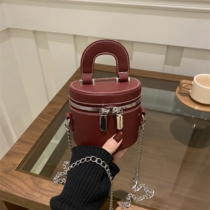 Mini burgundy cylinder chain bag in premium leather with silver metal strap on wood table