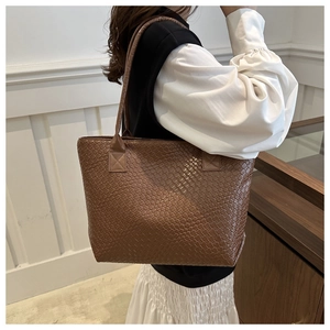 Model wearing a dark brown woven leather tote bag featuring a spacious interior design