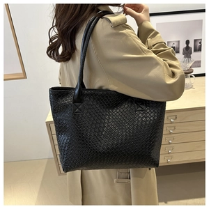 Close-up of black tote bag featuring premium woven leather texture and slender shoulder strap