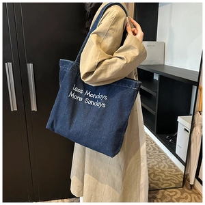 Detail of blue denim tote bag with white embroidery worn by model in trench coat