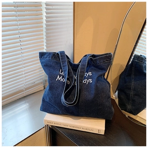 Detailed close-up of dark blue denim tote bag with Less Mondays More Sundays embroidery