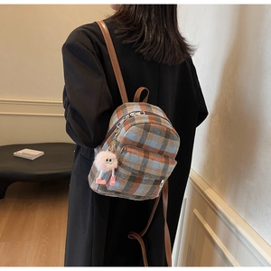 Detail of plaid mini backpack featuring a fuzzy pink charm and leather shoulder straps