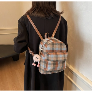Close-up of vintage plaid backpack with wool texture and a cute monster plush charm