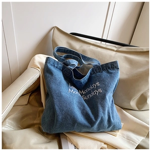 Detail of blue denim tote bag featuring white Less Mondays Sundays embroidery art