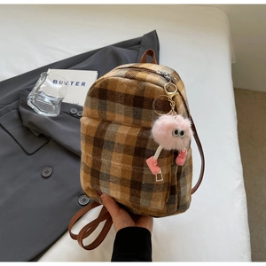 Dettaglio di mini zaino scozzese con ciondolo di peluche su uno sfondo di tessuto caldo
