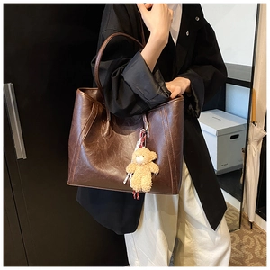 Detail of dark brown leather tote bag showing large capacity and plush bear charm