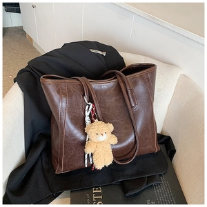 Detail of dark brown faux oil wax leather tote bag with a cute beige plush bear pendant