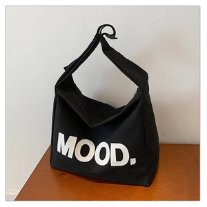Detail of black canvas tote bag featuring bold white MOOD text on wooden surface