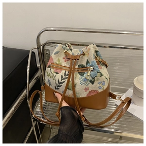 Detail of floral tapestry bucket bag featuring brown leather trim and golden zipper pocket
