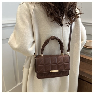 Detail of a dark brown quilted shoulder bag with a unique scrunchie handle and gold lock