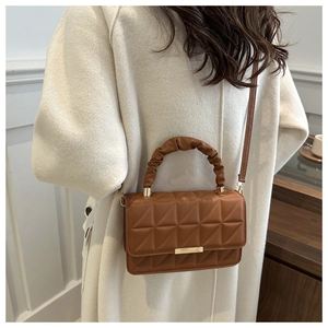 Close-up of brown quilted handbag with pleated handle on a model in white coat