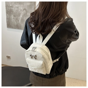 Close-up of a white textured mini backpack featuring a stylish silver metal bow detail