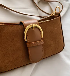 Dettaglio borsa baguette in camoscio marrone con fibbia a ferro di cavallo dorata e tracolla