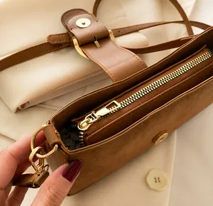 Dettaglio della cerniera in metallo dorato su una borsa sottobraccio in pelle scamosciata