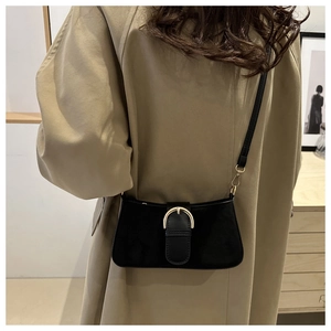 Dettaglio borsa baguette in camoscio nero con fibbia a D dorata su un trench kaki