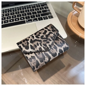Dettaglio del portafoglio a tre ante con stampa leopardata su scrivania in legno e caffè