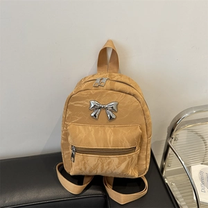 Brown mini backpack with crinkled texture and silver metal bow on leather bench