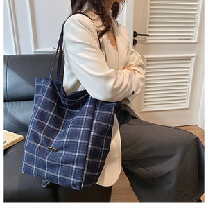 Detail of blue and white checkered canvas tote bag with metal logo and long shoulder strap