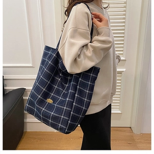 Detail of navy blue plaid tote bag showing the gold metal logo and fabric texture