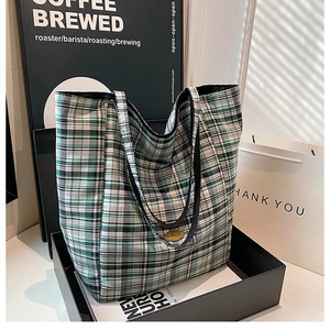 Close-up of green plaid tote bag featuring leather handles and a round metal logo plate