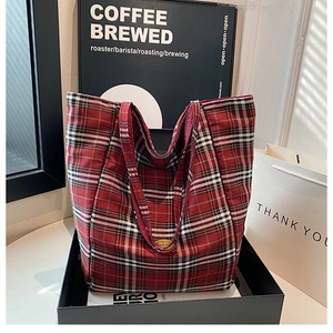 Detailed view of red plaid tote bag with metal snap closure inside a black gift box