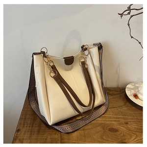 Detail of off-white tote bag featuring brown handles and chic woven shoulder strap