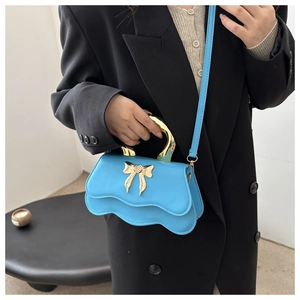 Detail of bright blue handbag with gold bow and metallic handle on black blazer