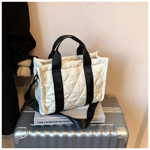 Detail of a cream quilted nylon tote bag placed on a silver metallic suitcase