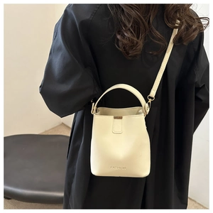 Detail of minimalist cream bucket bag showing smooth texture and crossbody strap on model