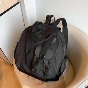 Minimalist black water-resistant nylon travel backpack with front flap pocket on a sofa