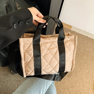 Chic beige quilted nylon handbag with black straps shown in a lifestyle hand-held shot