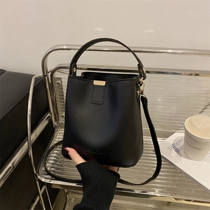 Modern black leather bucket bag with top handle and gold metal clasp on a shelf