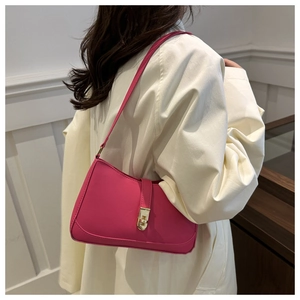 Detail of a rose red baguette bag with gold buckle worn over a beige trench coat