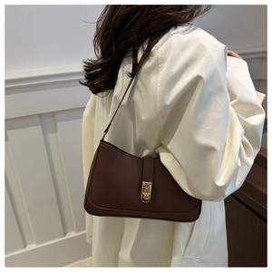 Detail of dark brown semi-moon shoulder bag with golden clasp worn on white coat