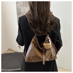 Detail of a brown leather tote bag with a cute plush bear charm and woven rope accent