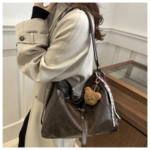 Detail of dark brown leather tote bag with plush bear charm and woven cord accessory