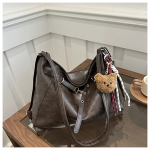 Detail of dark brown vintage leather tote with plush bear charm on a wooden table
