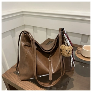 Detail of a brown vintage tote bag featuring a plush bear charm and plaid silk scarf decoration