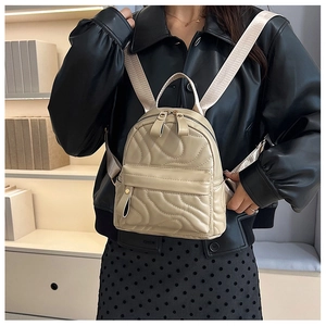 Close-up of quilted beige mini backpack with stylish wide fabric strap on a model