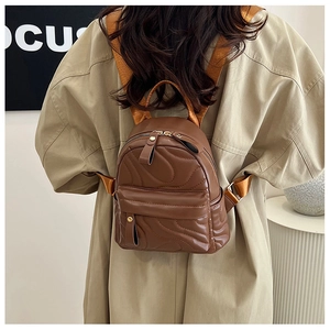 Close-up of brown quilted mini backpack with wave texture and golden zippers on model