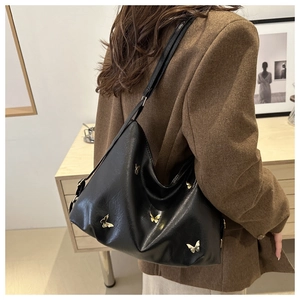 Close-up of black tote bag featuring gold butterfly ornaments and glossy PU leather