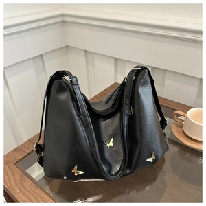 Close-up of black PU leather shoulder bag with golden butterfly accents on wooden table
